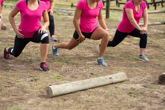 Grupo de mulheres todas vestindo camisetas rosa em uma sessão de treinamento de acampamento de inicialização, exercitando, esticando as pernas. Exercício de grupo ao ar livre, desafio saudável divertido. — Fotografia de Stock