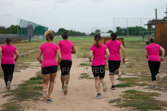 Grupo multi-étnico de mulheres todas vestindo camisetas cor-de-rosa em uma sessão de treinamento de campo de treinamento, exercendo, correndo em um campo. Exercício de grupo ao ar livre, desafio saudável divertido. — Fotografia de Stock