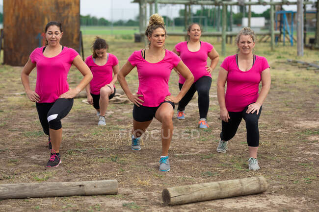 Multi-ethnic group of women all wearing pink t shirts at a boot camp training session, exercising, stretching their legs. Outdoor group exercise, fun healthy challenge. — Stock Photo
