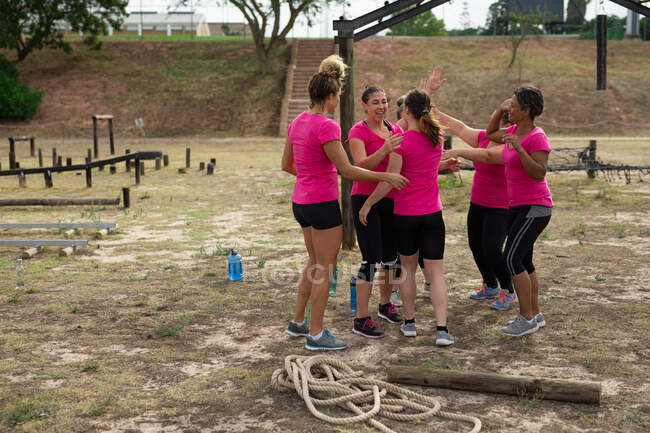 Gruppo multietnico di donne che indossano tutte magliette rosa in una sessione di allenamento di boot camp, che si allenano, si motivano a vicenda, fanno il tifo. Esercizio di gruppo all'aperto, divertente sfida sana. — Foto stock