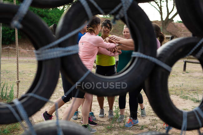 Groupe multi-ethnique de femmes portant toutes des t-shirts colorés lors d'une séance d'entraînement au camp d'entraînement, exerçant, motivant et empilant les mains. Exercice de groupe en plein air, défi sain amusant. — Photo de stock