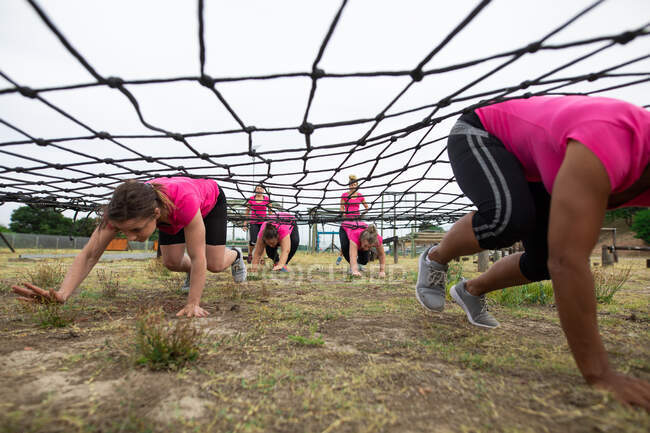 Multi-ethnische Gruppe von Frauen, alle tragen pinkfarbene T-Shirts bei einem Bootcamp-Training, turnen, kriechen unter einem Netz. Bewegung in der Gruppe, Spaß und gesunde Herausforderung. — Stockfoto