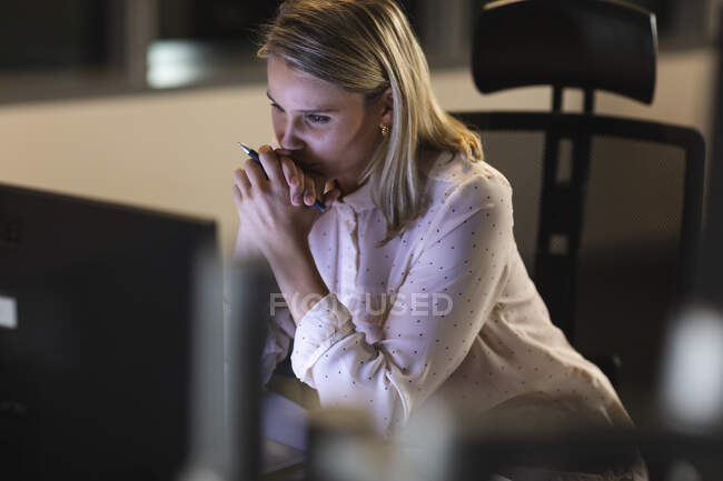 Mulher de negócios caucasiana trabalhando tarde da noite em um escritório moderno, sentado em uma mesa, usando um computador desktop. — Fotografia de Stock