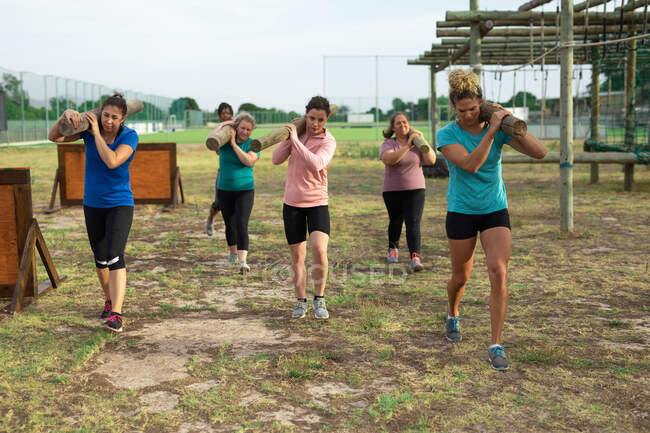 Gruppo multietnico di donne che indossano magliette colorate in una sessione di allenamento del campo di addestramento, esercitandosi, trasportando tronchi. Esercizio di gruppo all'aperto, divertente sfida sana. — Foto stock