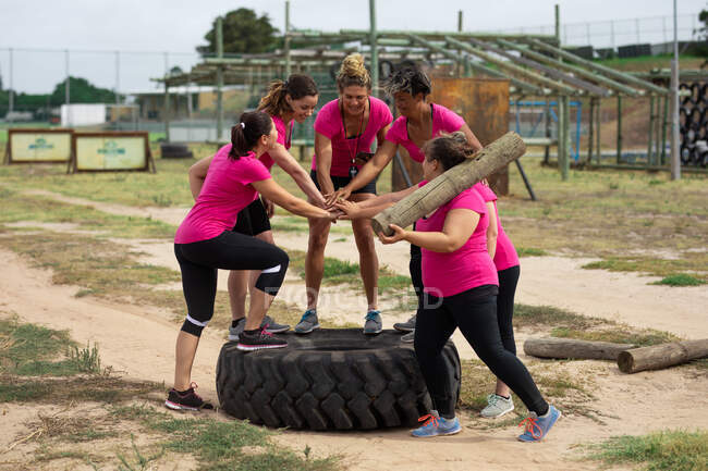 Gruppo multietnico di donne che indossano tutte magliette rosa in una sessione di allenamento di boot camp, esercitando mani motivanti e impilabili. Esercizio di gruppo all'aperto, divertente sfida sana. — Foto stock