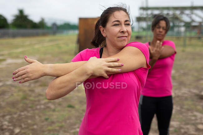 Gruppo multietnico di donne che indossano tutte magliette rosa in una sessione di allenamento di boot camp, esercitandosi, allungando le braccia. Esercizio di gruppo all'aperto, divertente sfida sana. — Foto stock