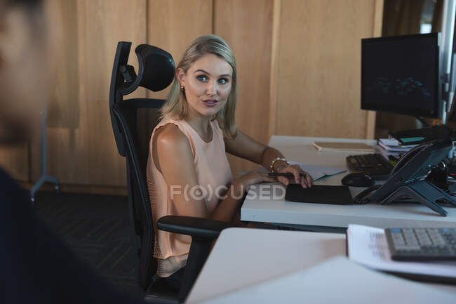 Asian and Caucasian businesswomen working late in the evening in a modern office, sitting at their desks and discussing their work. — Stock Photo