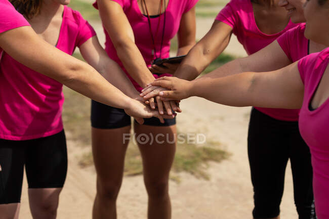 Grupo de mulheres todas vestindo camisetas rosa em uma sessão de treinamento de acampamento de inicialização, exercitando mãos motivadoras e empilhamento. Exercício de grupo ao ar livre, desafio saudável divertido. — Fotografia de Stock