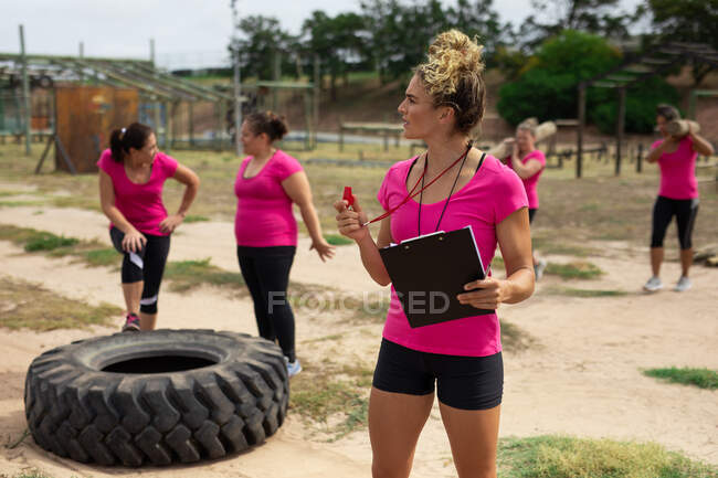 Мультиетнічна група жінок всі одягнені в рожеві футболки на тренувальному тренуванні в таборі чобіт, тренінги і їх диван з табличкою і свисток. Вправи на вулиці, приємне здоров 