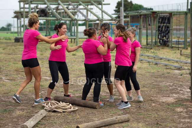 Grupo multi-étnico de mulheres todas vestindo camisetas cor-de-rosa em uma sessão de treinamento de campo de treinamento, exercitando-se, motivando umas às outras, dando altos cincos. Exercício de grupo ao ar livre, desafio saudável divertido. — Fotografia de Stock