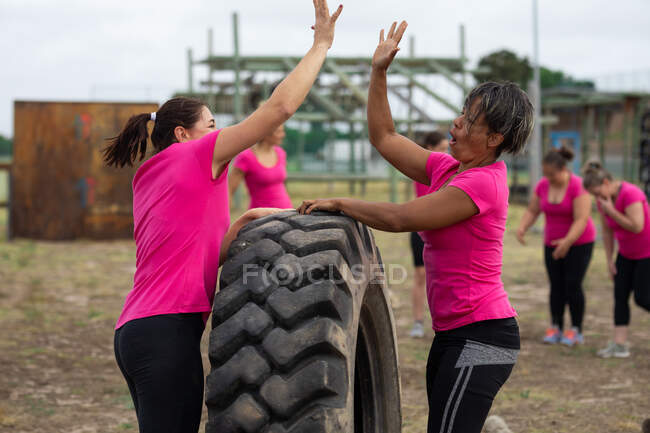 Grupo multi-étnico de mulheres todas vestindo camisetas cor-de-rosa em uma sessão de treinamento de campo de treinamento, exercitando-se, motivando umas às outras, dando altos cincos. Exercício de grupo ao ar livre, desafio saudável divertido. — Fotografia de Stock