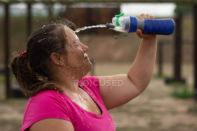 Жінка змішаної раси носить рожеву сорочку на тренувальному сеансі табору, займається фізичними вправами, відпочиває, поливає воду на обличчя. На відкритому повітрі група вправи, весело здоровий виклик . — стокове фото