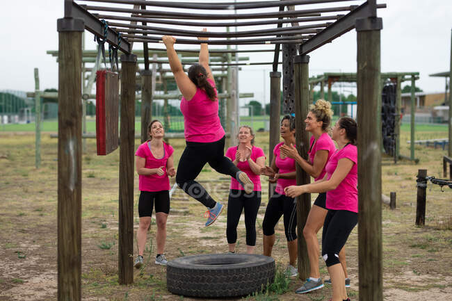 Multi-ethnische Frauengruppe, die alle pinkfarbene T-Shirts bei einem Bootcamp-Training tragen, trainieren, hängen an Affenstangen. Bewegung in der Gruppe, Spaß und gesunde Herausforderung. — Stockfoto