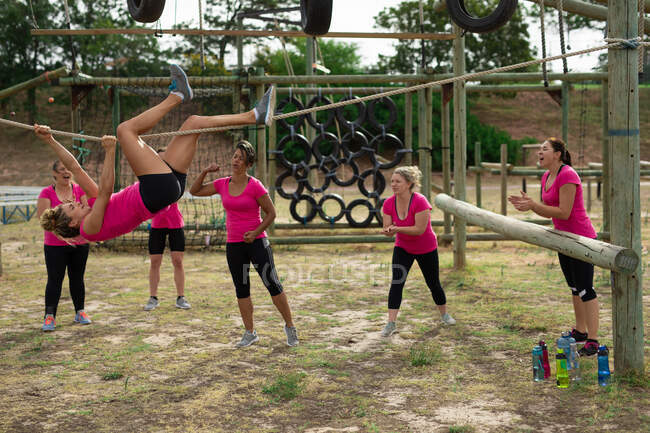 Подходит белой женщине в розовой футболке на тренировке в учебном лагере, тренируется, висит на веревке руками и ногами, группа мотивирует ее. Открытый групповые упражнения, весело здоровый вызов. — стоковое фото