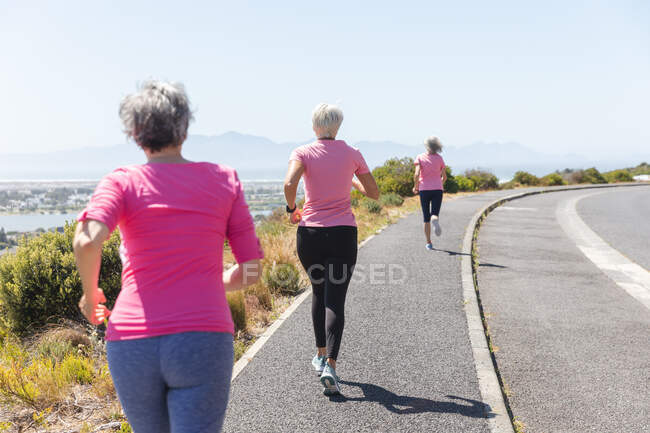 Gruppe kaukasischer Freundinnen, die an einem sonnigen Tag mit blauem Himmel Sport treiben, Rennen laufen und rosa Sportbekleidung tragen. — Stockfoto