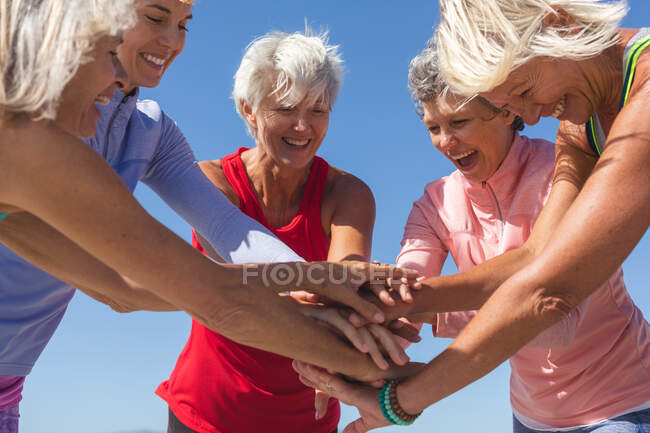 Gruppe glücklicher kaukasischer Freundinnen, die an einem sonnigen Tag am Strand Sport treiben, lächeln, stehen und sich zusammentun. — Stockfoto