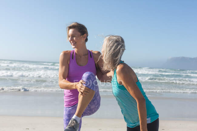 Gruppe kaukasischer Freundinnen, die an einem sonnigen Tag am Strand Sport treiben, Yoga praktizieren und sich mit dem Meer im Hintergrund dehnen. — Stockfoto