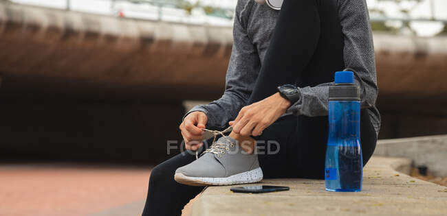 Fit woman wearing sportswear exercising outdoors in the city, tying shoelaces taking break in urban park, water bottle next to her. Urban lifestyle exercise. — Stock Photo