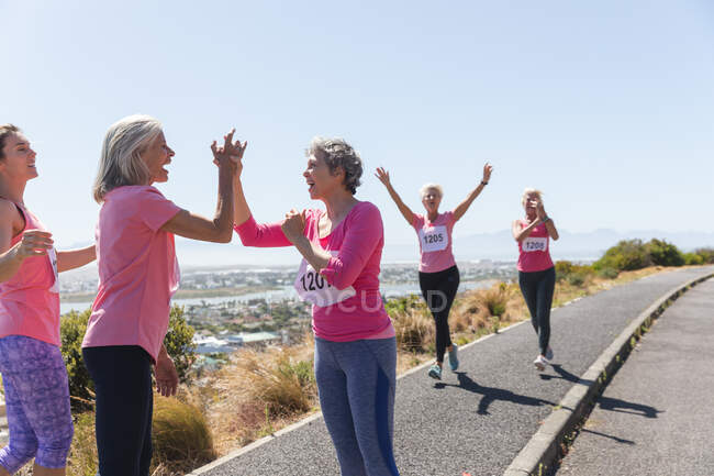 Grupo de amigas caucasianas que gostam de se exercitar em um dia ensolarado, comemorando após a corrida, vestindo números e sorrindo. — Fotografia de Stock