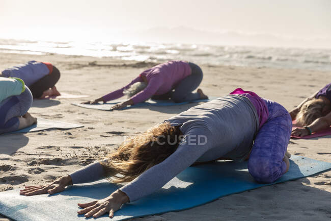 Група друзів з Кавказу у сонячний день насолоджуються вправами на пляж, займаючись йогою і сидячи в позиції йоги.. — стокове фото