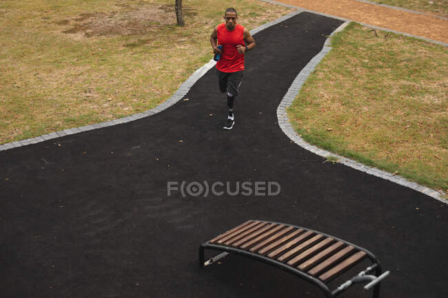 Hombre de raza mixta discapacitado con una pierna protésica, haciendo ejercicio en un parque, llevando una botella de agua. Fitness discapacidad estilo de vida saludable. - foto de stock
