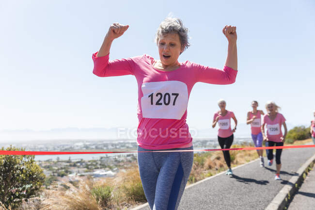 Gruppe kaukasischer Freundinnen, die es genießen, an einem sonnigen Tag Sport zu treiben, Rennen zu laufen und Nummern zu tragen, in Richtung Ziellinie zu rennen und zu feiern. — Stockfoto