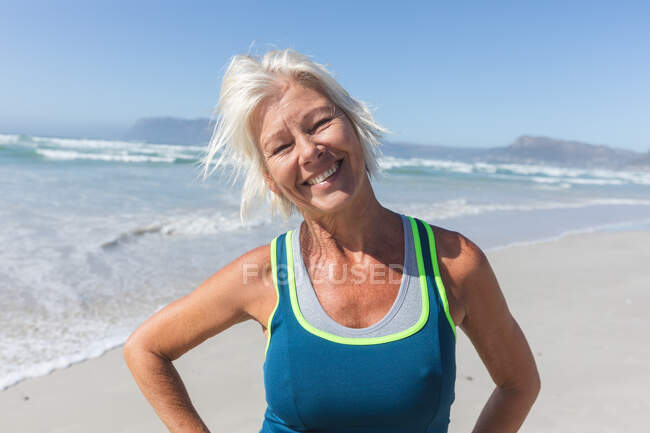 Portrait of a senior Caucasian woman enjoying exercising on a beach on a sunny day, smiling, standing and looking at camera with sea in the background. — Stock Photo