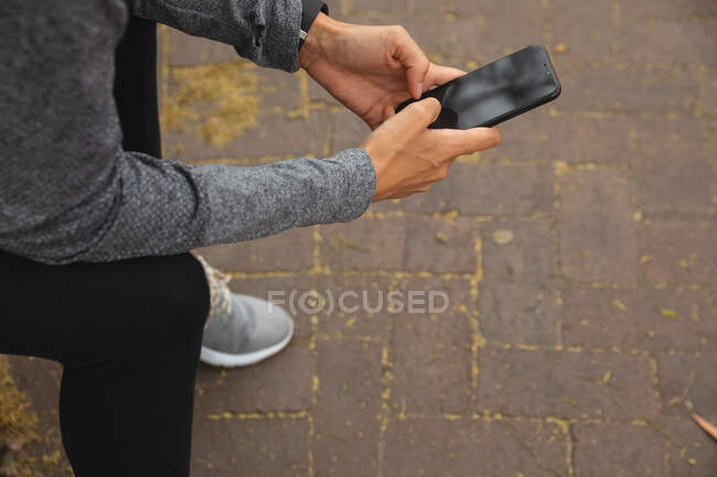Підійде жінка в спортивному одязі, займається спортом на вулиці міста, сидячи на перерві, використовуючи свій смартфон у міському парку. Міський спосіб життя вправи . — стокове фото