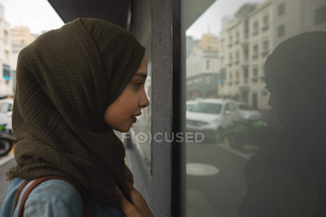Жінка змішаної раси в хіджабі і близько на ходу в місті, стоячи на вулиці, дивлячись у вікно магазину. Комп'ютерний сучасний спосіб життя . — стокове фото