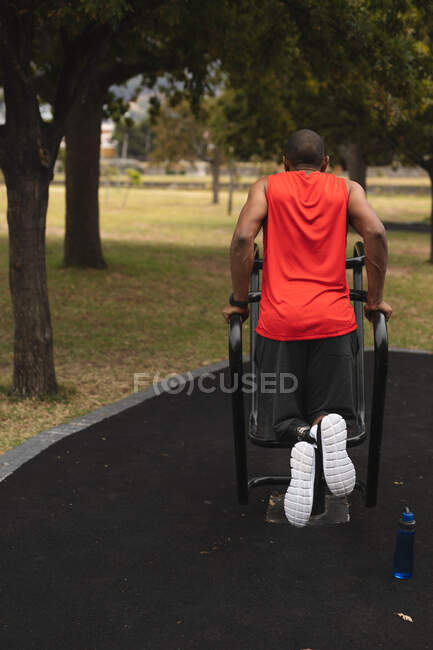 Rückansicht eines behinderten Mischlingsrennfahrers mit Beinprothese, der in einem Park in einer Outdoor-Turnhalle trainiert und Klimmzüge macht. Fitness Behinderung gesunder Lebensstil. — Stockfoto