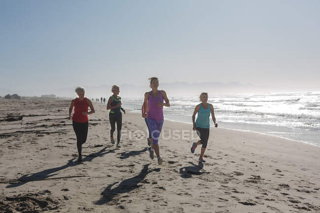 Gruppe kaukasischer Freundinnen, die an einem sonnigen Tag an einem Strand Sport treiben, am Meer laufen und lächeln. — Stockfoto