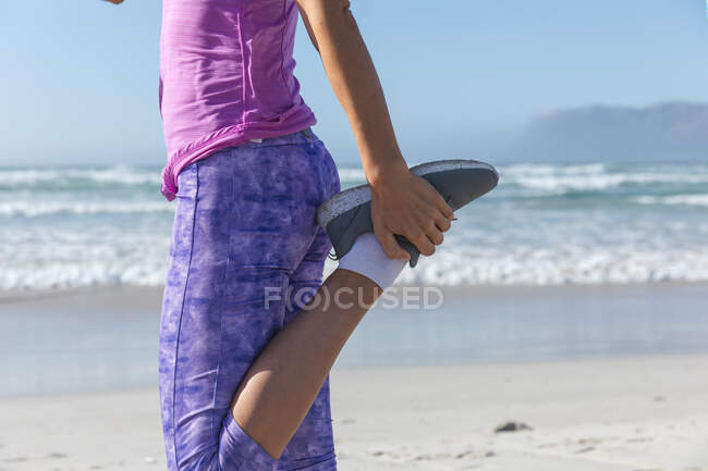 Середина жінки насолоджується фізичними вправами на пляжі в сонячний день, практикує йогу і розтягується з морем на задньому плані . — стокове фото
