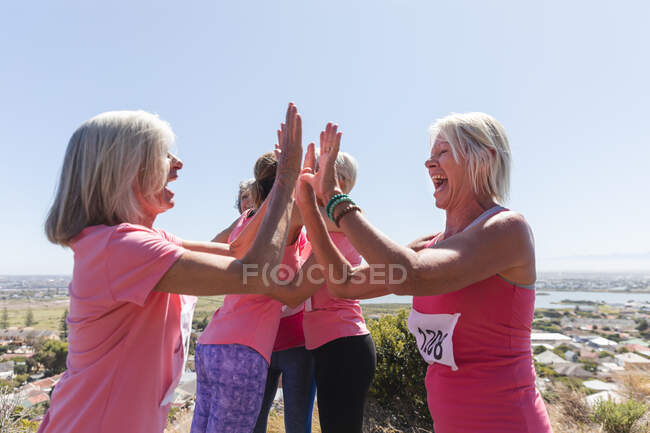Gruppo di amiche caucasiche che si esercitano in una giornata di sole, festeggiano dopo la corsa, indossano numeri e sorridono, danno il cinque. — Foto stock