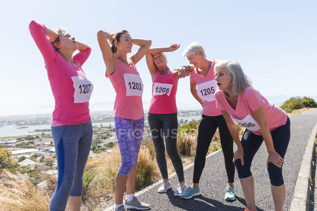 Group of Caucasian female friends enjoying exercising on a sunny day, taking a break after running race, wearing numbers and pink sportswear. — Stock Photo