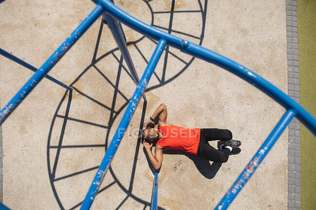 Overhead view of a disabled mixed race man with a prosthetic leg  exercising at an outdoor gym by the coast, doing sit ups in the sun beside the gym equipment. Fitness disability healthy lifestyle. — Stock Photo