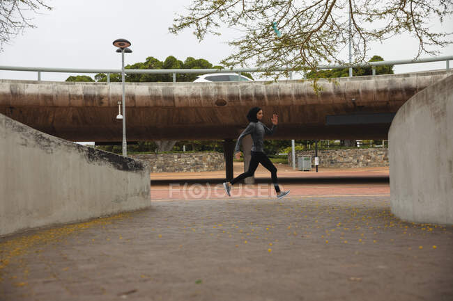 Fit mulher de raça mista vestindo hijab e sportswear exercitando ao ar livre na cidade, correndo em um parque urbano. Exercício urbano. — Fotografia de Stock