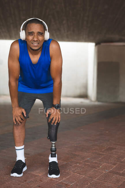 Behinderter Mischlingsrennfahrer mit Beinprothese, der in einem Stadtpark trainiert und kabellose Kopfhörer trägt, die eine Pause einlegen. Fitness Behinderung gesunder Lebensstil. — Stockfoto