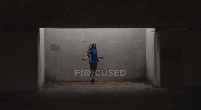 Disabled mixed race man with a prosthetic leg, working out in an urban park, wearing hooded top, skipping with skipping rope. Fitness disability healthy lifestyle. — Stock Photo