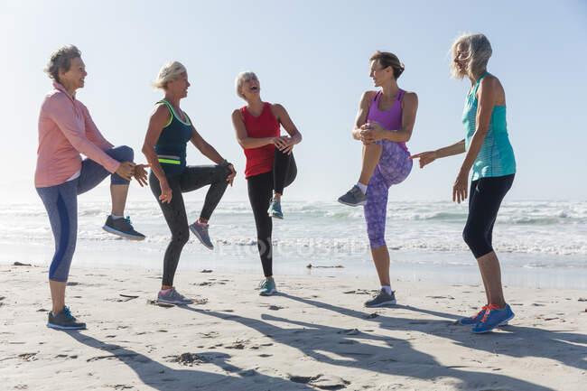 Gruppe kaukasischer Freundinnen, die an einem sonnigen Tag am Strand Sport treiben, Yoga praktizieren und sich mit dem Meer im Hintergrund dehnen. — Stockfoto