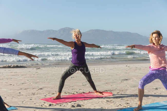 Gruppe kaukasischer Freundinnen, die an einem sonnigen Tag am Strand Sport treiben, Yoga praktizieren und in Yogaposition stehen. — Stockfoto