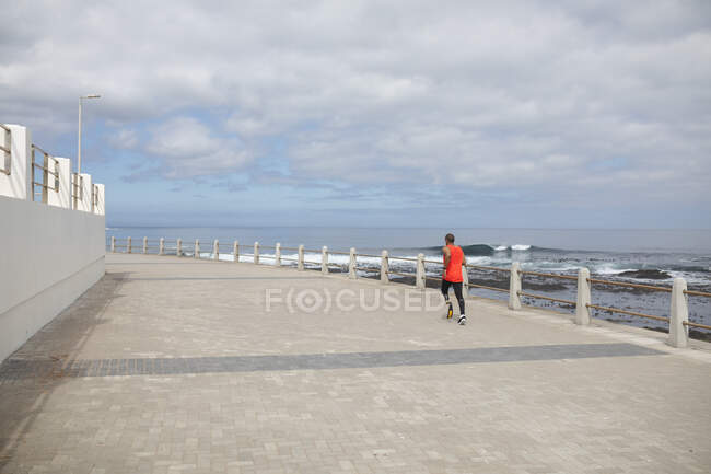 Homme de race mixte handicapé avec une jambe prothétique et une lame de course à pied travaillant sur la côte en cours d'exécution sur une promenade au bord de la mer. Fitness handicap mode de vie sain. — Photo de stock