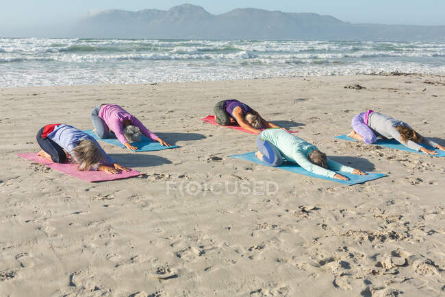 Gruppe kaukasischer Freundinnen, die an einem sonnigen Tag am Strand Sport treiben, Yoga praktizieren und in Yogaposition sitzen. — Stockfoto