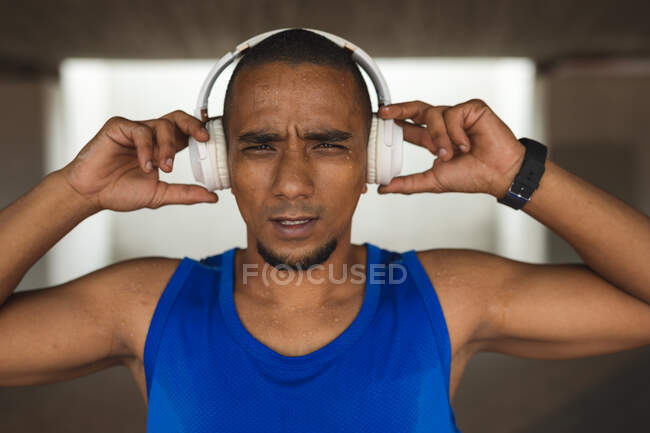 Portrait of mixed race man working out in an urban park, wearing sportswear, smartwatch and wireless headphones, taking a break. Fitness strength healthy lifestyle. — Stock Photo