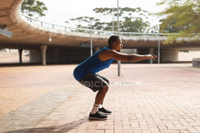 Disabled mixed race man with a prosthetic leg, working out in an urban park, leaning against wall, stretching his leg. Fitness disability healthy lifestyle. — Stock Photo