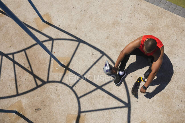 Blick von oben auf einen behinderten Mixed-Race-Mann mit prothetischer Laufklinge, der in einem Outdoor-Fitnessstudio trainiert und sich auf dem Boden ausruht. Fitness Behinderung gesunder Lebensstil. — Stockfoto