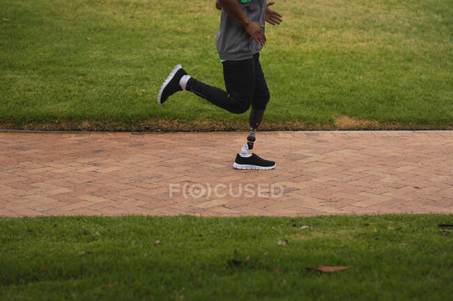 Low section of disabled man with a prosthetic leg, working out in an urban park, wearing sportswear running on a path. Fitness disability healthy lifestyle. — Stock Photo