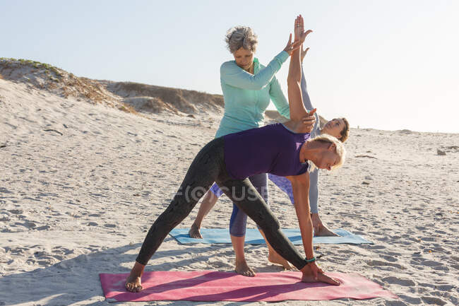 Gruppo di amiche caucasiche che si esercitano su una spiaggia in una giornata di sole, praticano yoga e si trovano in posizione yoga. — Foto stock