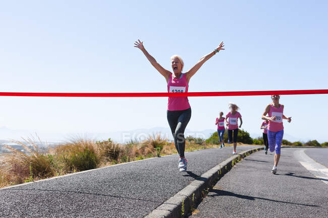 Gruppe kaukasischer Freundinnen, die es genießen, an einem sonnigen Tag Sport zu treiben, Rennen zu laufen und Nummern zu tragen, in Richtung Ziellinie zu rennen und zu feiern. — Stockfoto