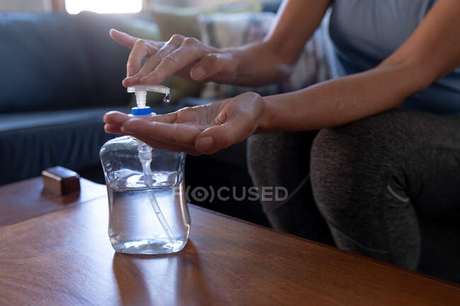 Woman enjoying time at home, social distancing and self isolation in quarantine lockdown, sitting in living room on sofa, disinfecting hands protecting from Covid 19 coronavirus. — Stock Photo