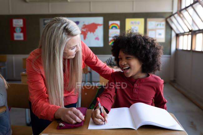 Insegnante caucasica femminile che insegna a un ragazzo di razza mista durante la lezione. Istruzione primaria distanza sociale sicurezza sanitaria durante la pandemia di Covid19 Coronavirus. — Foto stock